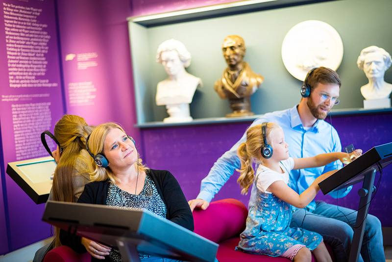 Familie sitzt mit Kopfhörern im Museum und hört Musik von Richard Wagner